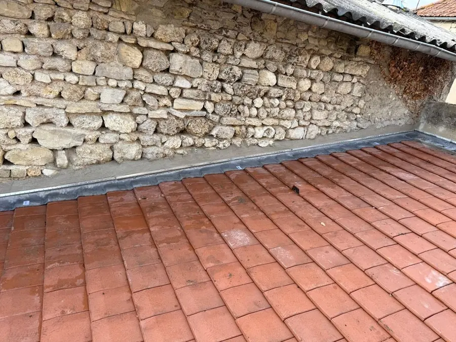 Couverture en tuiles et solin contre un mur en pierre